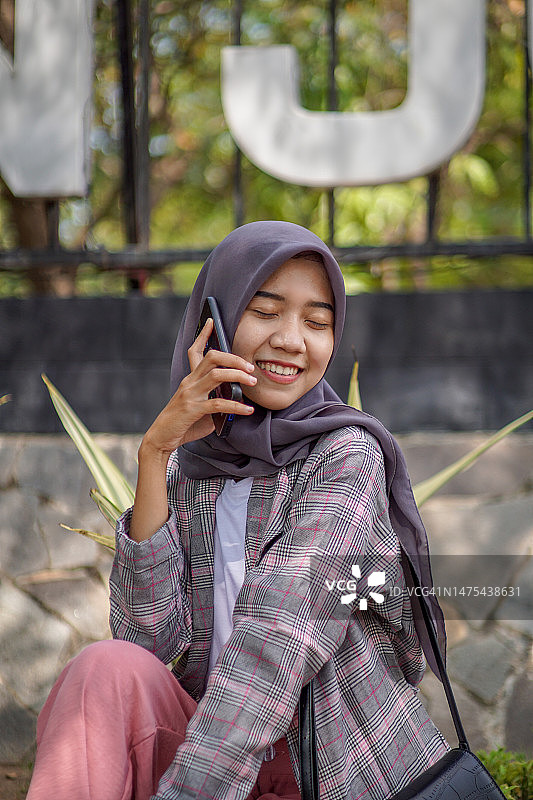 美丽的头巾穆斯林学生打电话给她的朋友在公园用智能手机图片素材