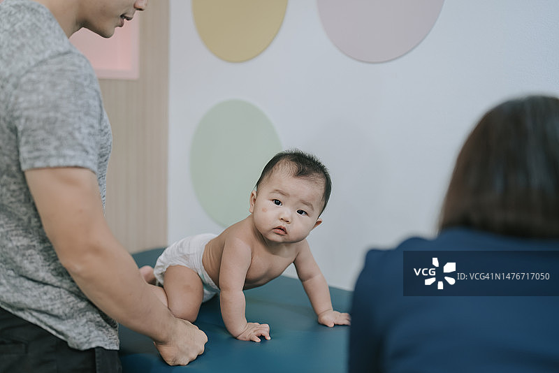 好奇的亚裔中国男婴爬在婴儿换尿布垫上看着相机图片素材