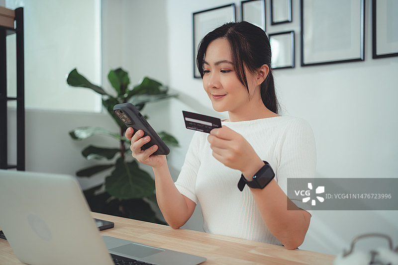 亚洲女性喜欢网上购物，持有信用卡，在家办公时使用智能手机在线支付。图片素材