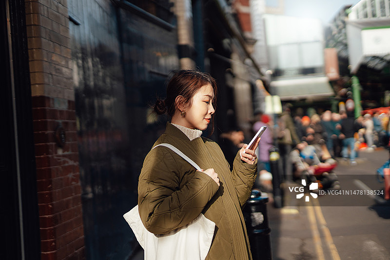 年轻的亚洲女子在城市街道上使用智能手机图片素材