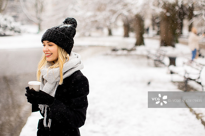 年轻女子温暖的衣服享受在雪与外卖咖啡杯图片素材