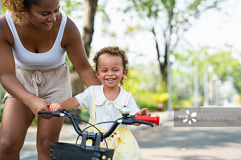 妈妈教她的小女儿如何在公园里骑自行车。图片素材