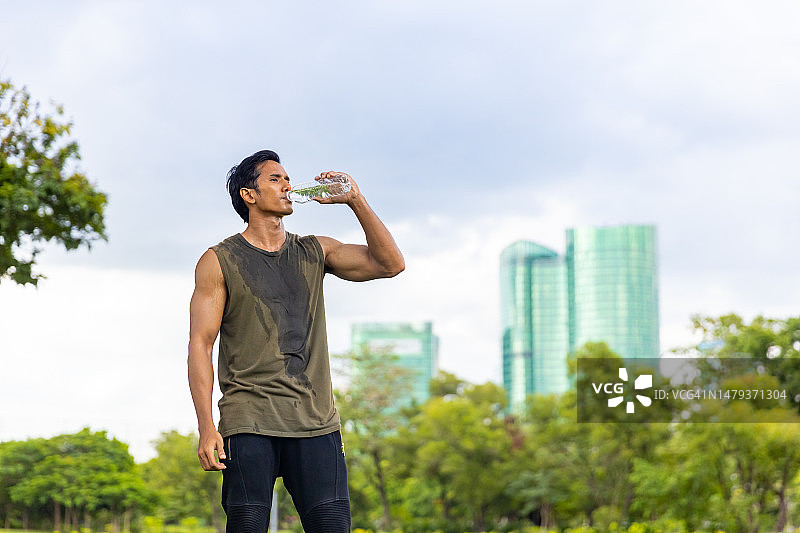 亚洲男子早上在公园慢跑时喝水。图片素材