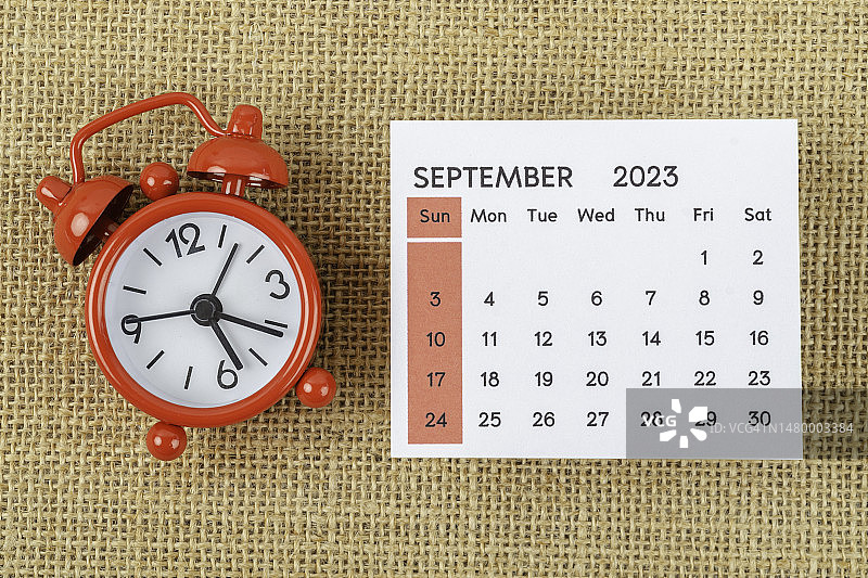 日历台2023:9月是组织者计划和截止日期的月份，并在粗麻布背景上设置闹钟。图片素材