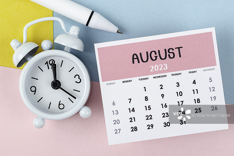 日历桌2023:8月是组织者用闹钟和白笔在双色纸背景下计划和截止日期的月份。图片素材