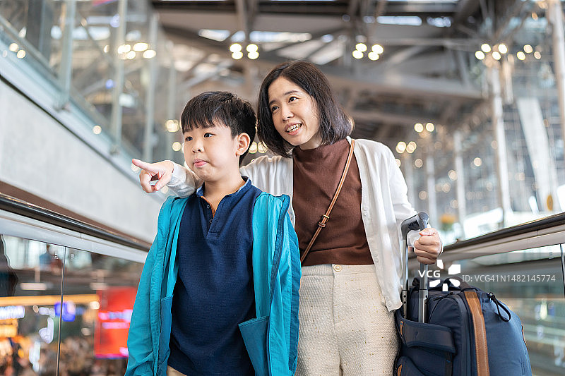 通过出国旅行积累经验。母子俩站在自动扶梯上，举手指着前方，儿子看着。一名女子拿着护照和行李，准备去机场办理登机手续。假期旅行。图片素材