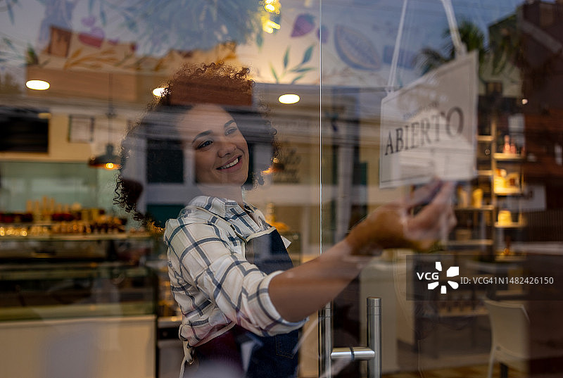 快乐的女服务员在咖啡馆里挂着西班牙语的开放标语图片素材