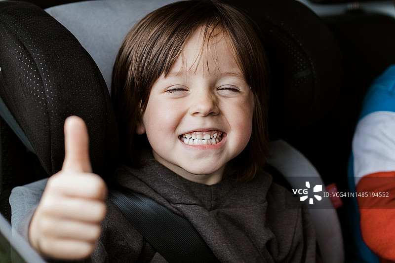 快乐微笑的婴儿坐在汽车座椅上，竖起大拇指。图片素材