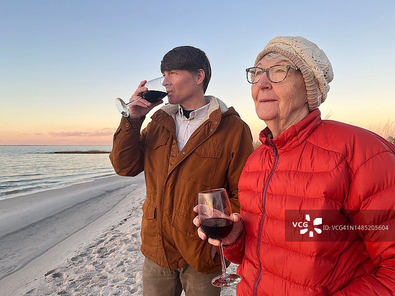 成年的儿子和年长的成年母亲在冬季的海滩上享受日落和葡萄酒，在家庭周末度假。丹吉尔的声音。图片素材