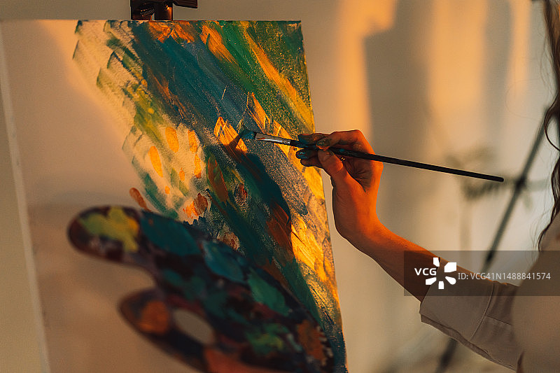 画家手里拿着调色板，在阳光下用油画颜料在画布上作画图片素材
