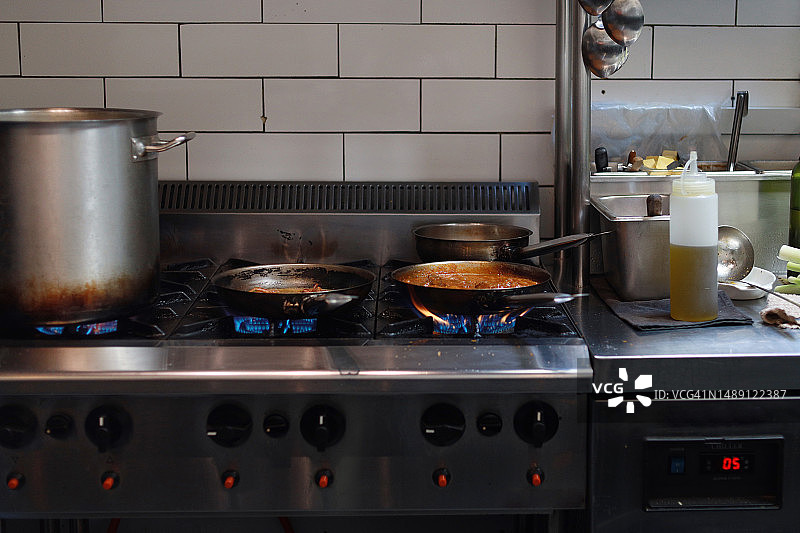 锅碗瓢盆放在煤气灶上，在商业厨房里烹饪食物。图片素材