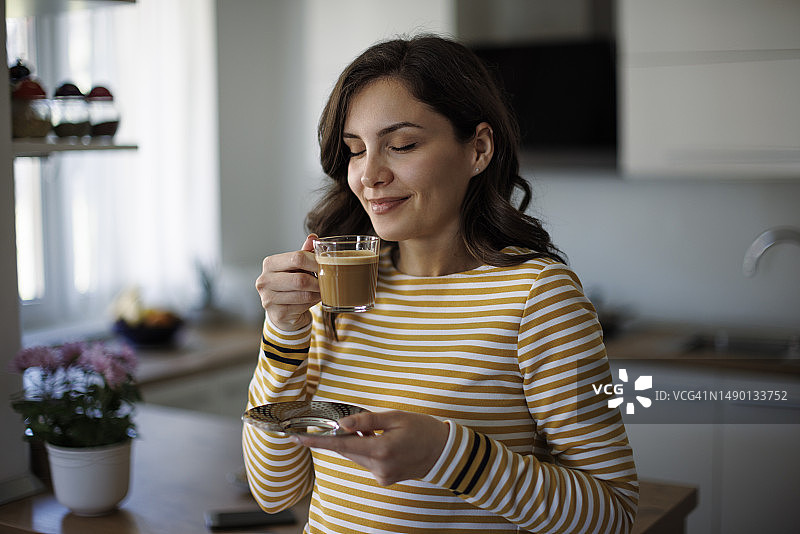 年轻微笑的女人在家里喝咖啡图片素材