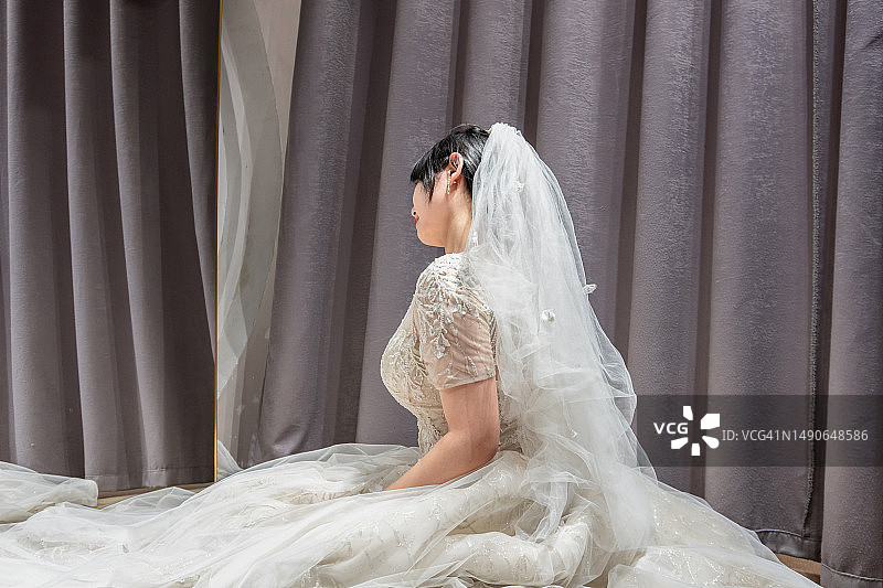 穿着白色蕾丝婚纱的年轻亚洲女子坐在地板上图片素材
