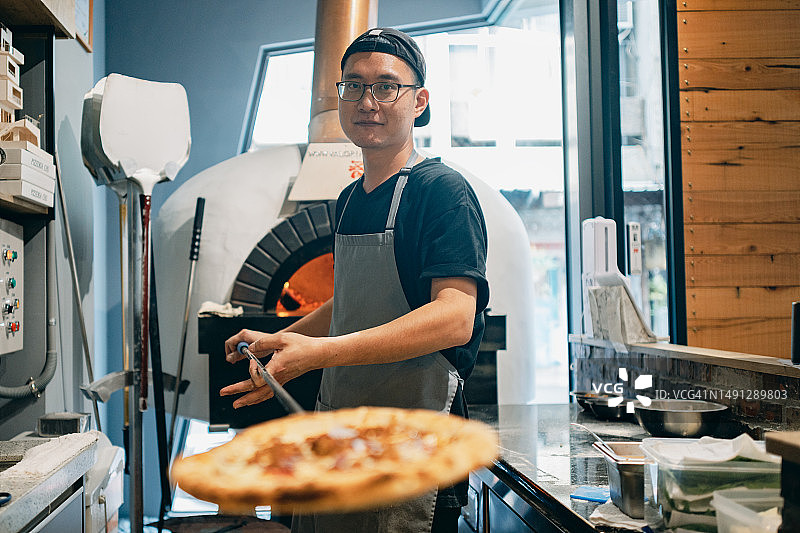 一名亚洲男子正在餐厅厨房工作，用柴火烤炉准备传统的披萨。图片素材