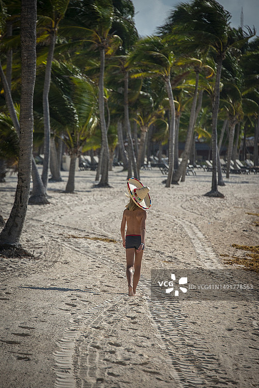 戴着宽边帽的小男孩走在墨西哥里维埃拉玛雅的海滩上图片素材