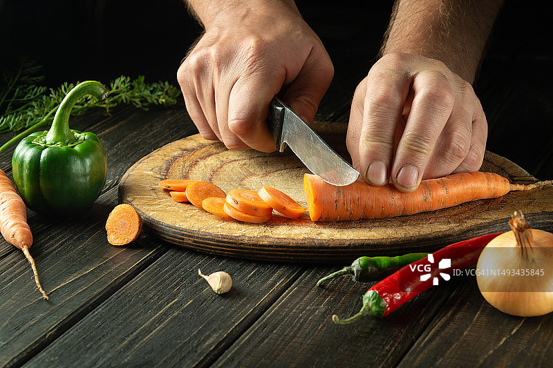 厨师把胡萝卜切成小块放在菜板上，准备素食午餐或晚餐。厨房桌子上的一套蔬菜。图片素材