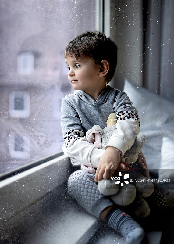 德国汉诺威，一个男孩坐在家里的窗台上望着窗外图片素材