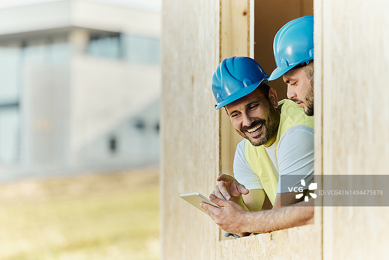 快乐的建筑工人在建筑结构上使用触摸板。图片素材