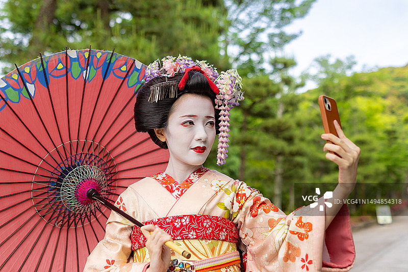 日本艺伎在京都祗园公园的铺砌街道上自拍，手持日本传统纸伞遮阳图片素材