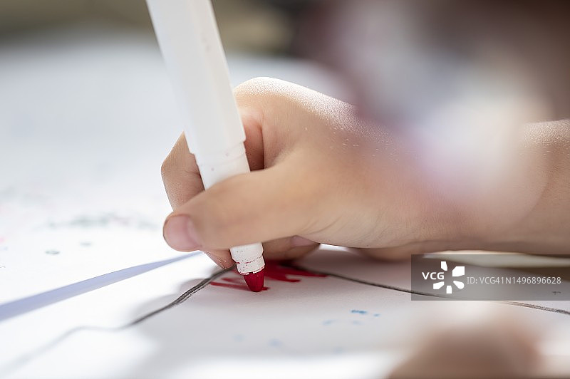 一个小孩用红色记号笔在纸上画画图片素材