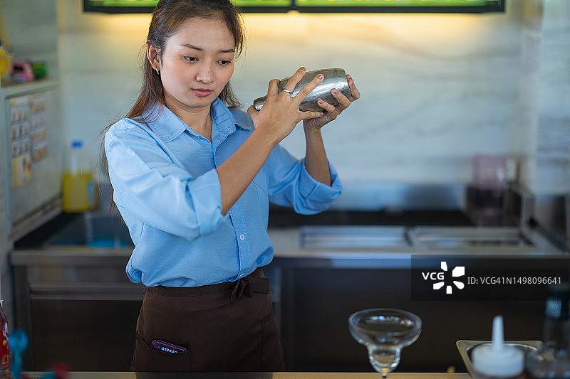 亚洲女调酒师在餐厅吧台准备鸡尾酒。图片素材
