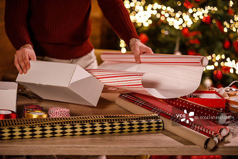 一个年轻人正在测量他需要多少包装纸来包装一个圣诞礼盒图片素材
