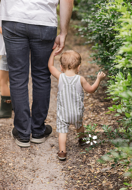 2023年夏天，佛罗里达州西棕榈滩花园，一个1岁的小男孩，浅棕色短发和棕色眼睛，穿着鼠尾草绿和白色条纹工装裤，休闲夏装图片素材