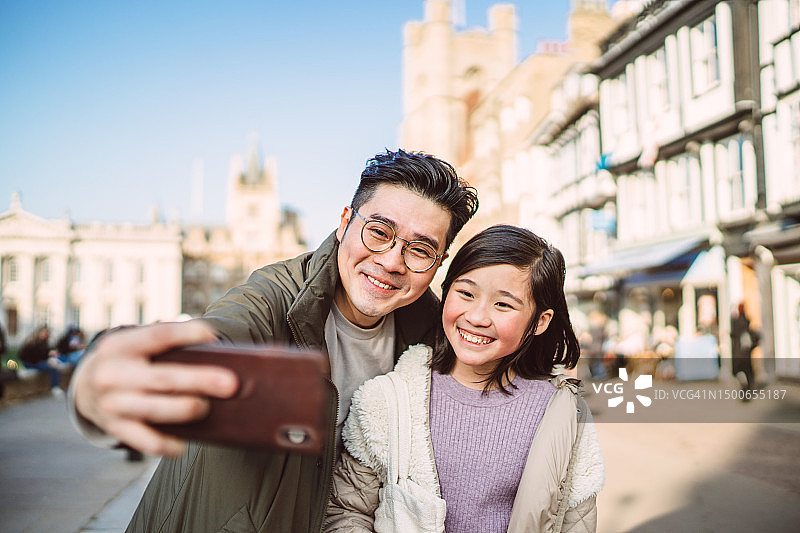 爸爸和女儿在镇上探索时愉快地用智能手机自拍图片素材