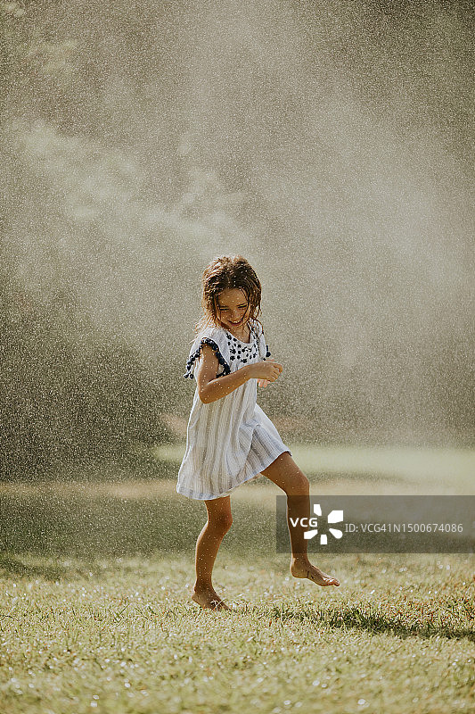 可爱的小女孩在灌溉洒水器下玩耍，黑山图片素材