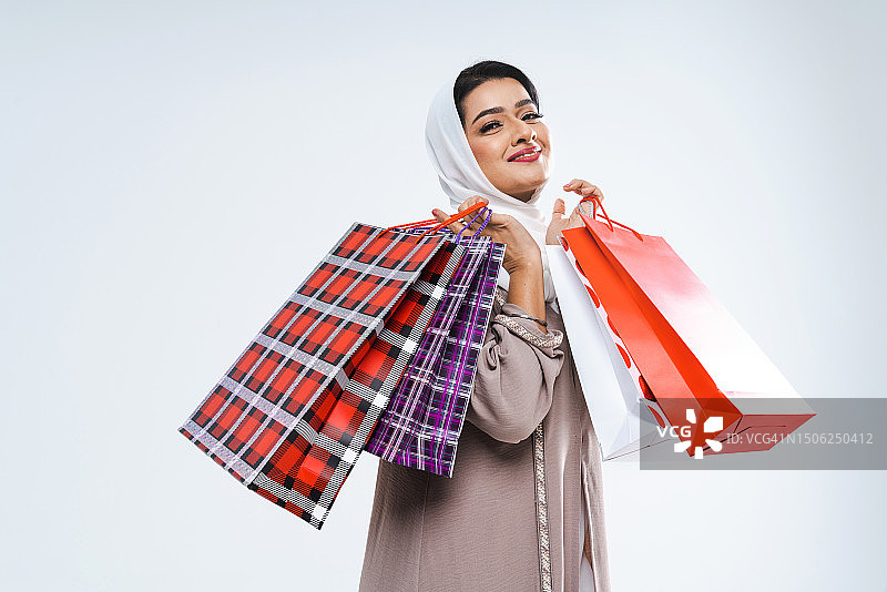 阿拉伯联合酋长国，一个微笑的年轻女子拿着白色背景的购物袋图片素材