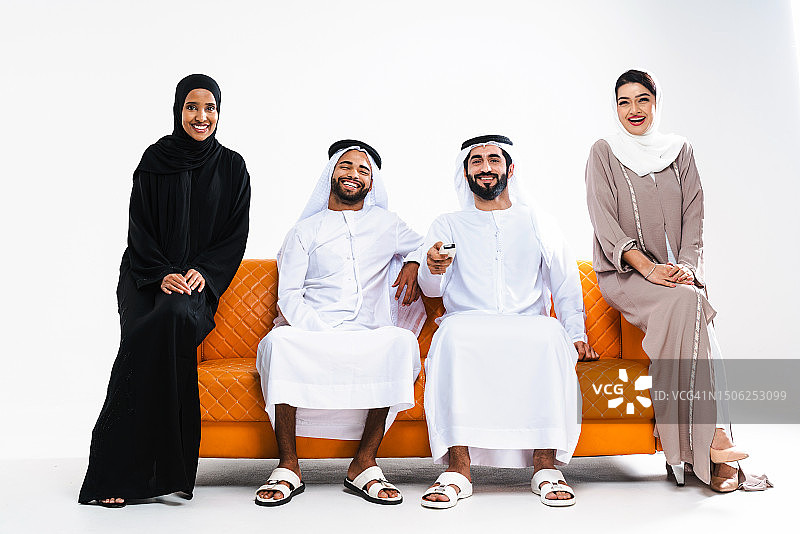 美丽的阿拉伯中东朋友，穿着传统的酋长国服装，坐在白色背景下的橙色沙发上图片素材