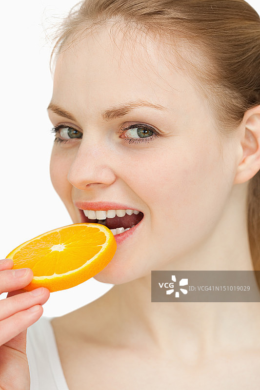 一个女人把一个橙子片在她的嘴的特写图片素材