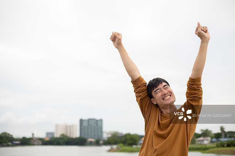 一名亚洲男子在桥上高举双手，以城市景观为背景图片素材