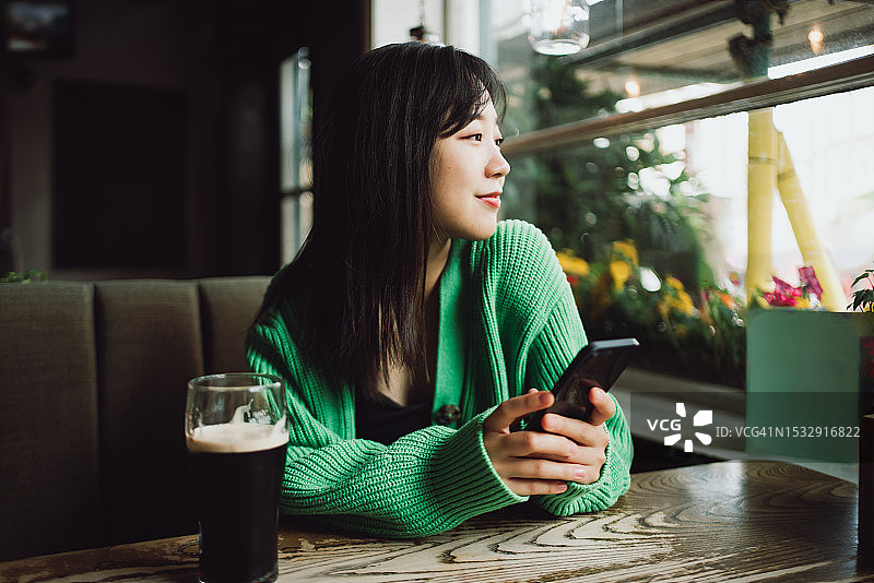 一个亚洲美女在餐厅里拿着她的智能手机向外看图片素材