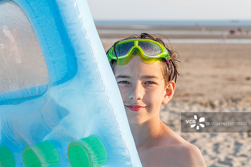 一个男孩抱着充气床垫站在海边的沙滩上图片素材