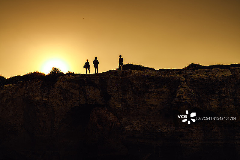 夕阳下，一小群人站在海边的悬崖上。旅行和冒险的概念。图片素材