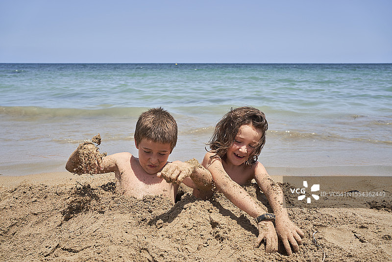 哥哥和姐姐一起在沙滩上玩泥巴，埋在沙滩上晒太阳图片素材
