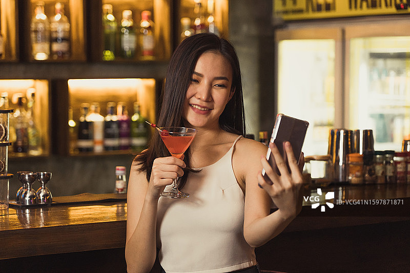 一名亚洲女子在酒吧喝威士忌时自拍。图片素材