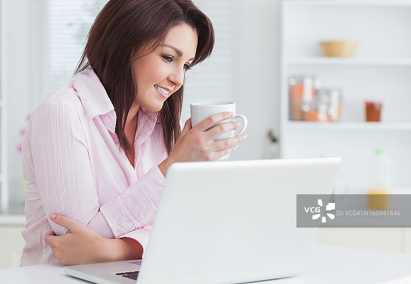 微笑的女人拿着咖啡杯用笔记本电脑图片素材