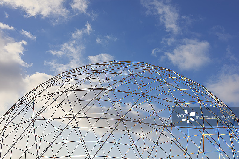 在华沙郊区的一个废弃游乐园里，一个巨大的球形圆顶，在多云的天空下，有一个未覆盖的三角形金属晶格壳图片素材