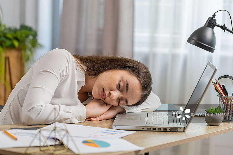 无聊困倦的年轻女商人在笔记本电脑上工作，在家里办公室睡着了图片素材