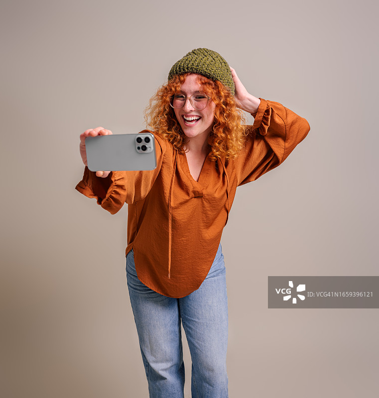 开朗美丽的年轻女子，一头卷曲的红发，在后台用智能手机自拍图片素材