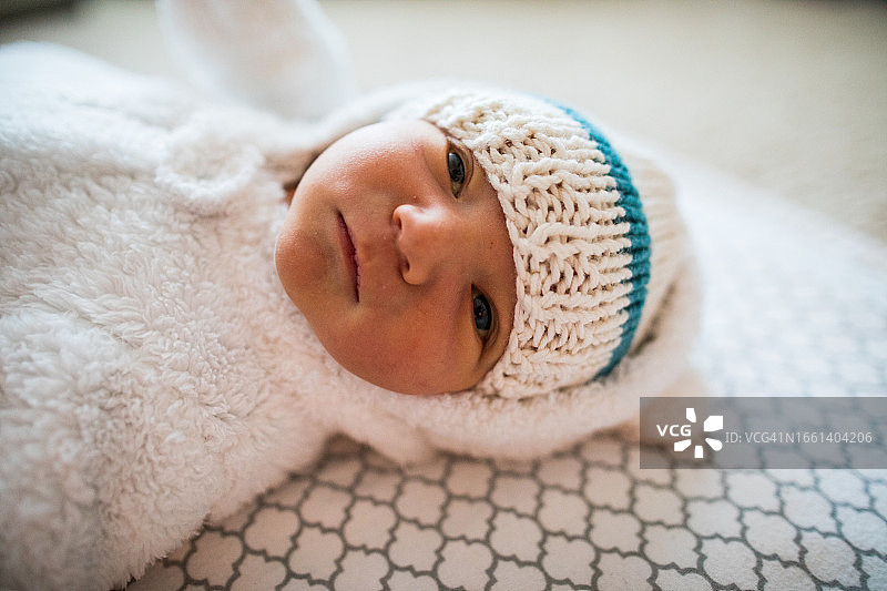 可爱的婴儿穿着白色的无边帽和舒适的连体衣的侧视图图片素材