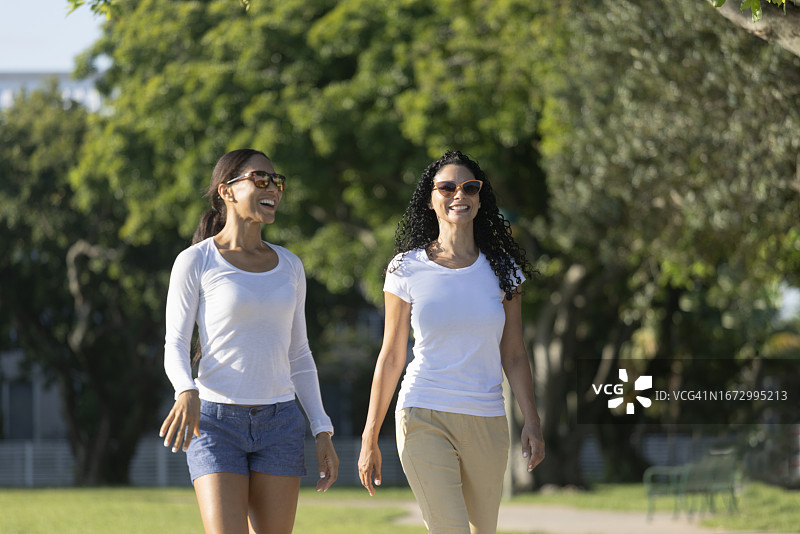 两名千禧一代的女性穿着休闲服，在公园里散步。图片素材