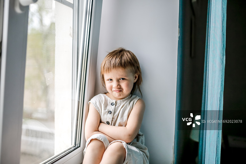 一个穿着亚麻工装裤站在窗边，情绪激动，生气的年轻女孩。图片素材