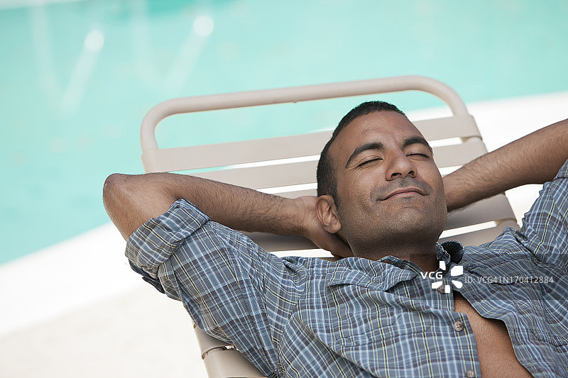 男子在泳池边的躺椅上休息图片素材