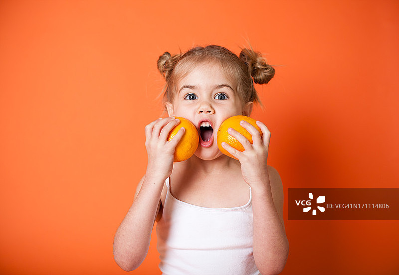 一个小女孩把两个橙子举到她面前图片素材