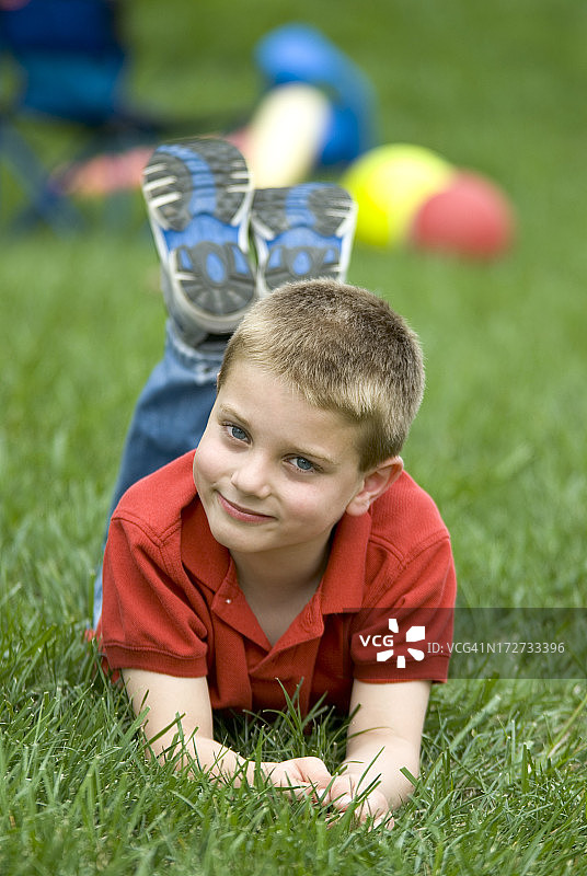 快乐的小男孩在草地上拿着玩具，翘着脚。图片素材