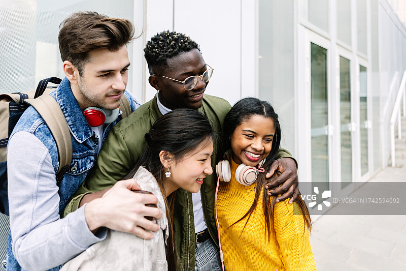 一群年轻的多种族朋友站在一起，在户外表现出团结。千禧一代的学生在大学大楼上互相拥抱。友谊的概念。图片素材