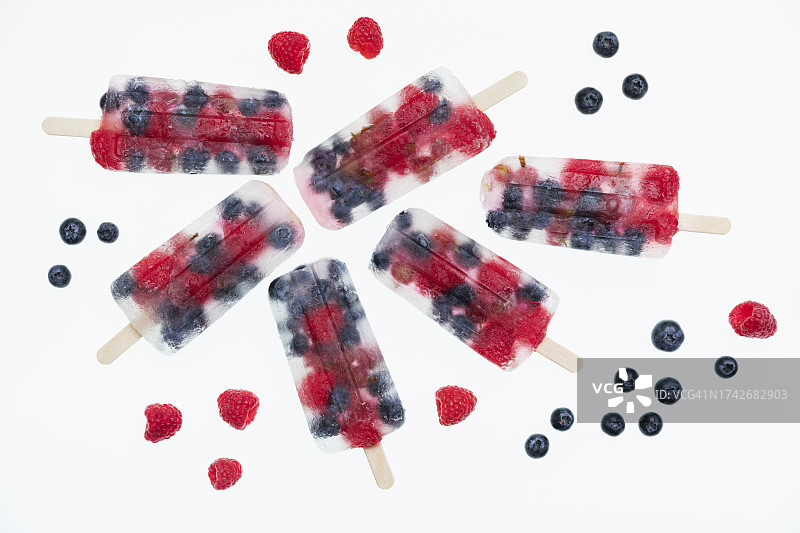 工作室拍摄的自制冰棒与新鲜的覆盆子，蓝莓和醋栗躺在白色的背景图片素材
